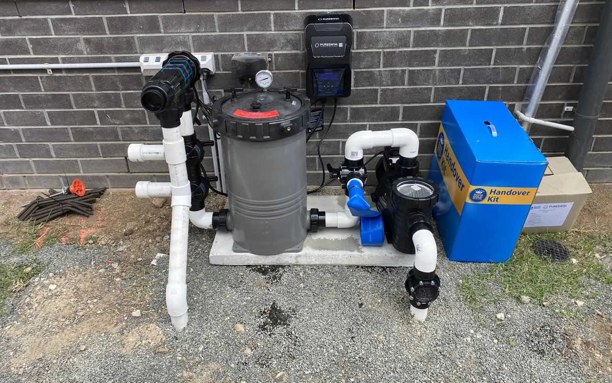 PureSwim mineral chlorinator cell and controller, cartridge filter and pump on the equipment pad of a new MFP pool, with the handover kit box beside them
