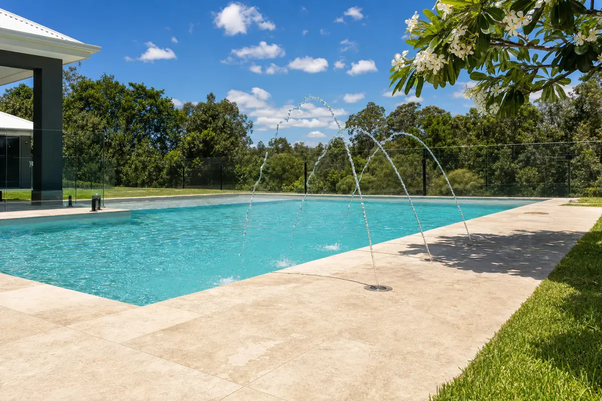 Deck jets arcing from travertine paving into a rectangular fibreglass pool on a sunny day