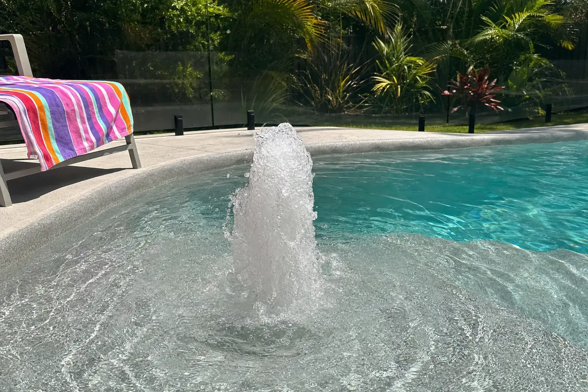 Foam jet bubbling up from the shallow ledge of a fibreglass pool in summer