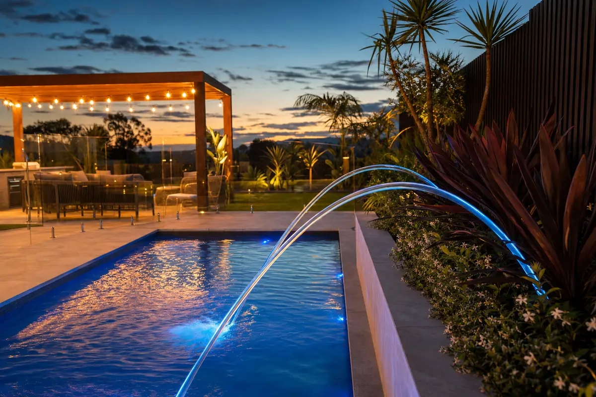 Laminar jets throwing clear LED-lit arcs of water into a pool at dusk