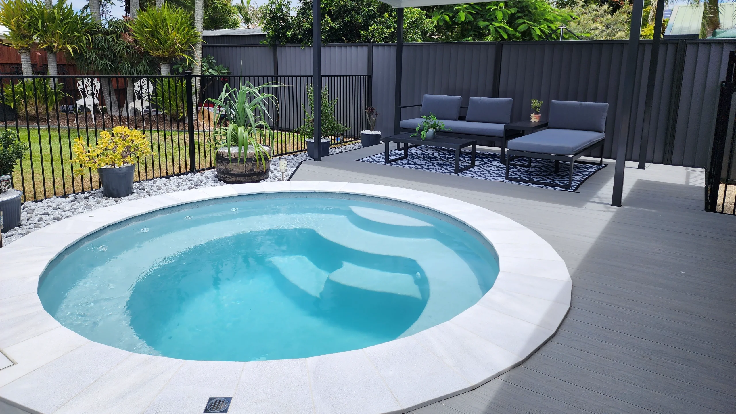 Small round fibreglass plunge pool with white paved coping set into a timber-look deck beside a lounge area