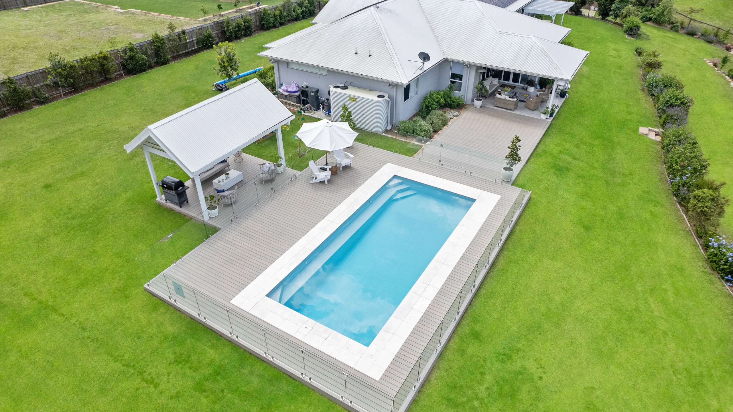 Aerial view of a rectangular fibreglass pool with white coping set into a composite deck beside a home