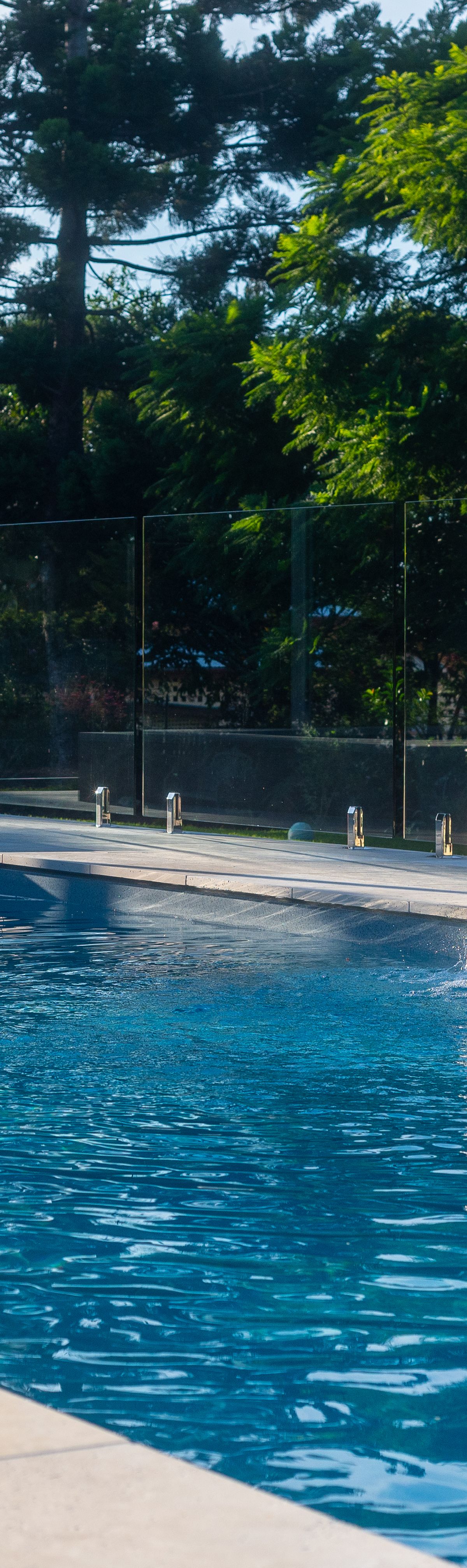 Travertine-clad water feature wall with two staggered LED water blades sheeting into a fibreglass pool and spa in Booval