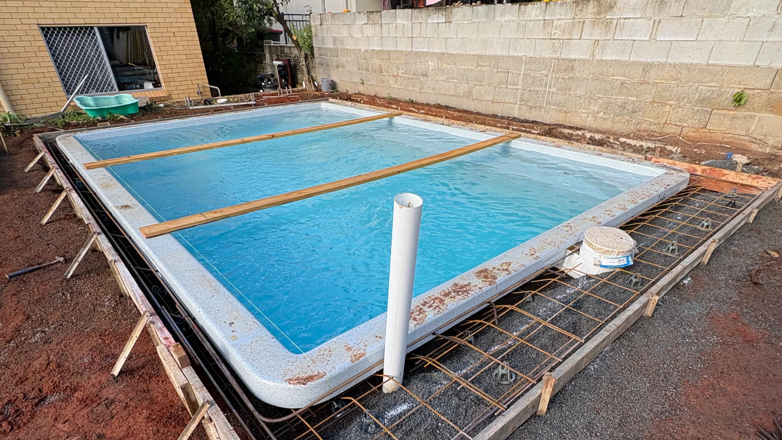 Rectangular fibreglass pool shell filled with water sits in its excavated site, ready for the surrounding concrete collar to be poured