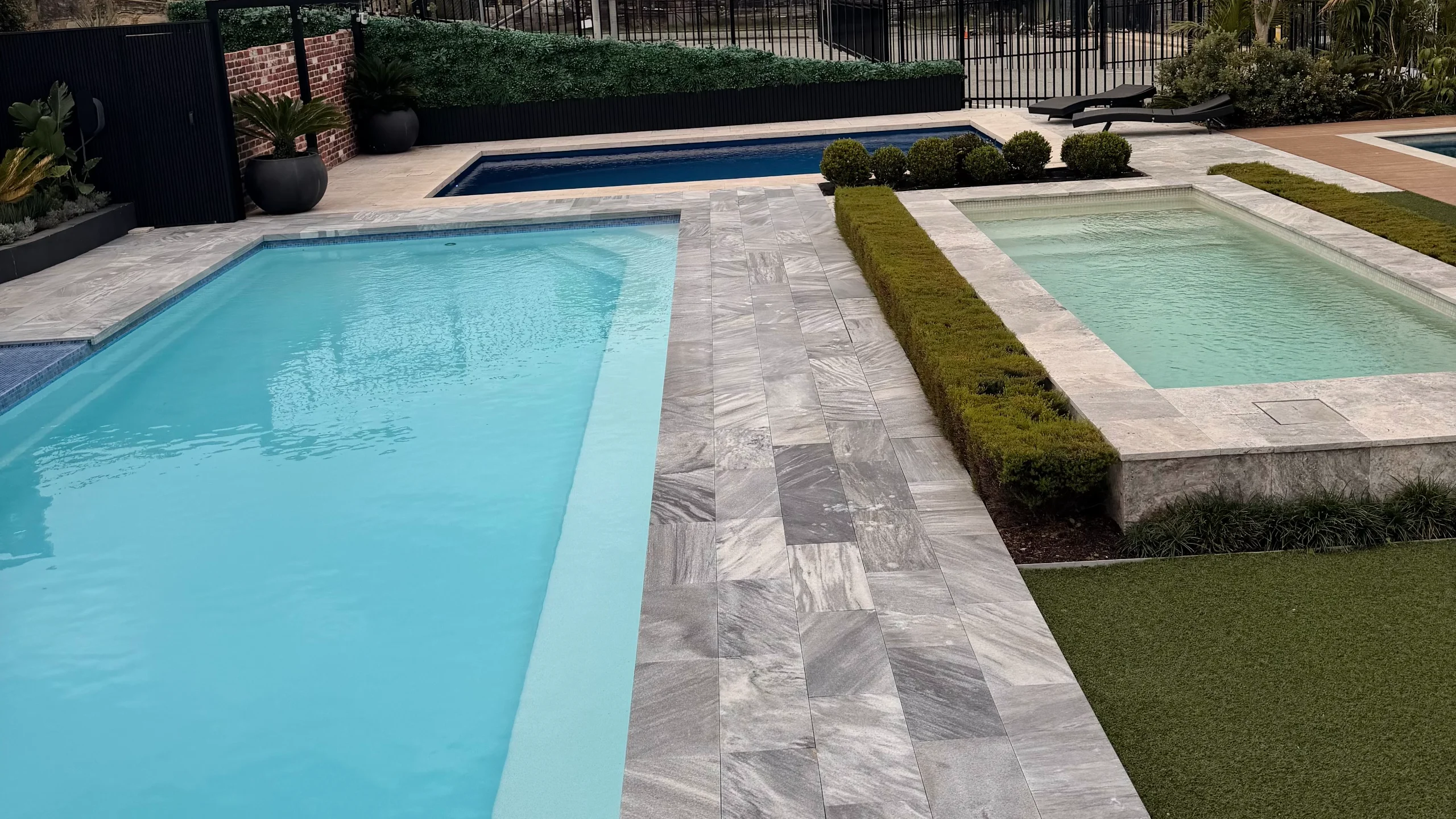 Three fibreglass display pools — pale blue rectangle, dark-water pool and raised plunge pool with grey stone-look paving