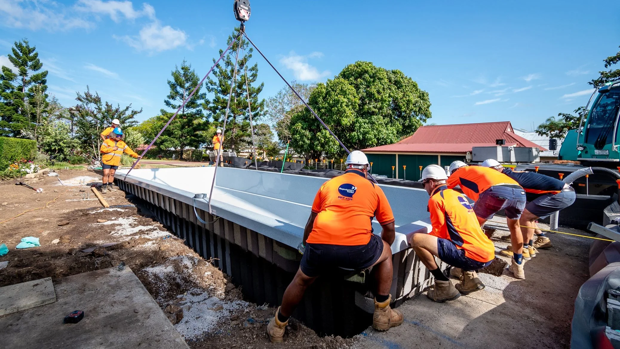 The MFP Easy team guiding a craned Aqua Technics fibreglass pool shell into a freshly dug excavation on site