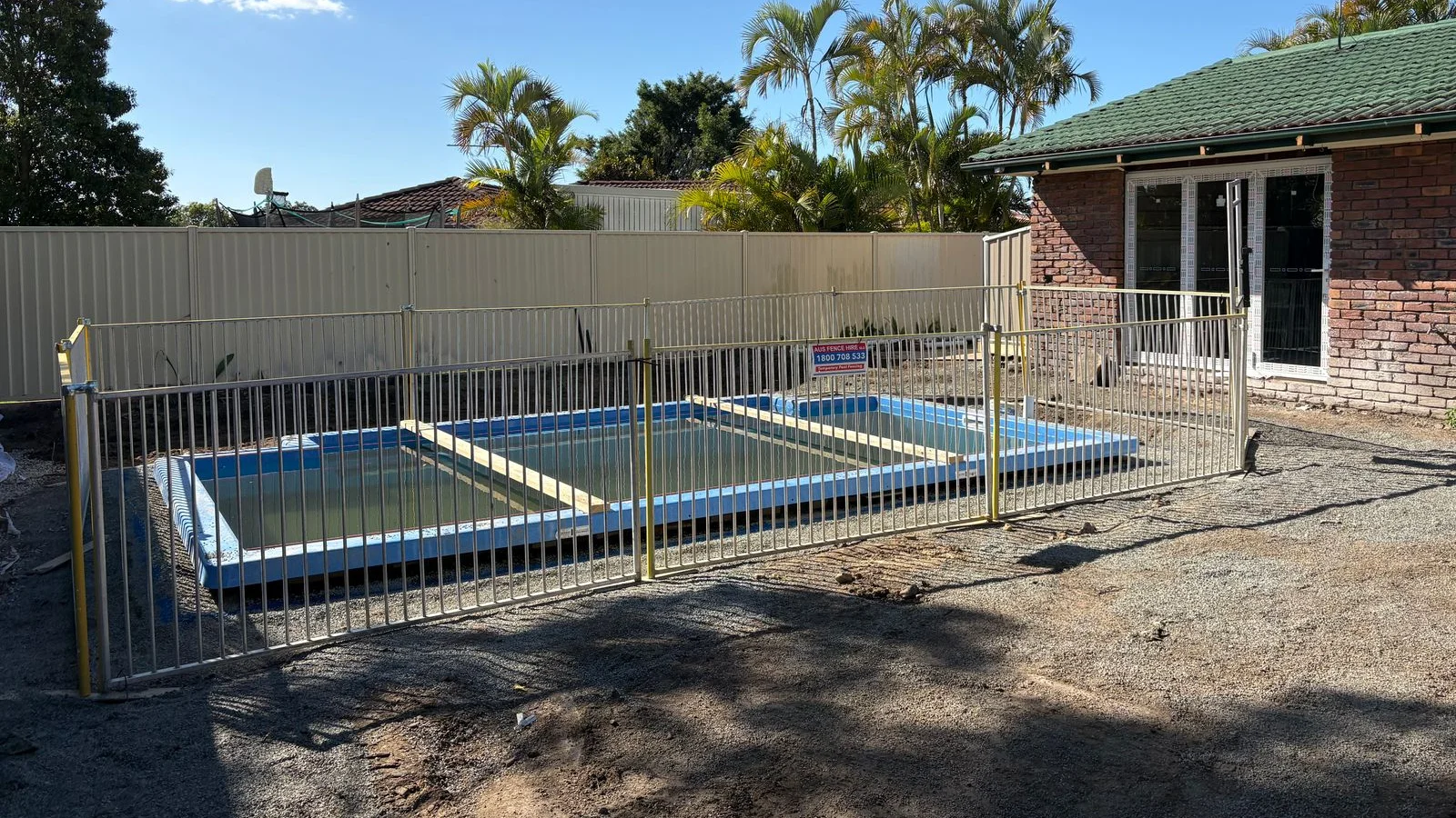 Rectangular fibreglass pool shell being installed with temporary safety fencing during a backyard build