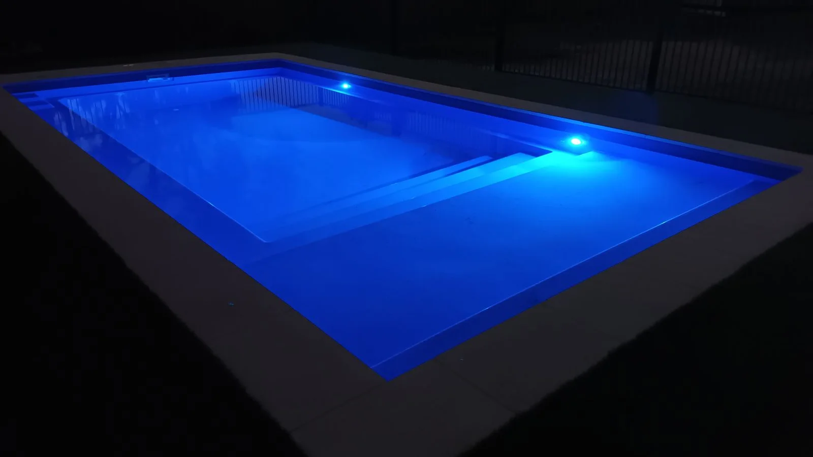 Fibreglass pool illuminated at night by blue LED lights along the wall and step edge