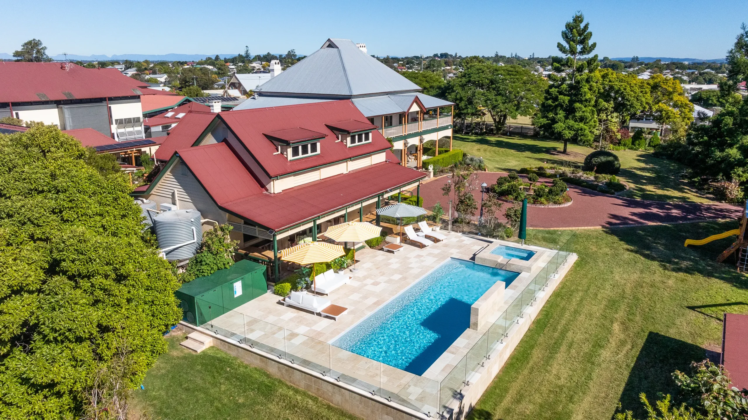 Inground fibreglass pool with glass fencing and travertine surround beside a grand Queensland home
