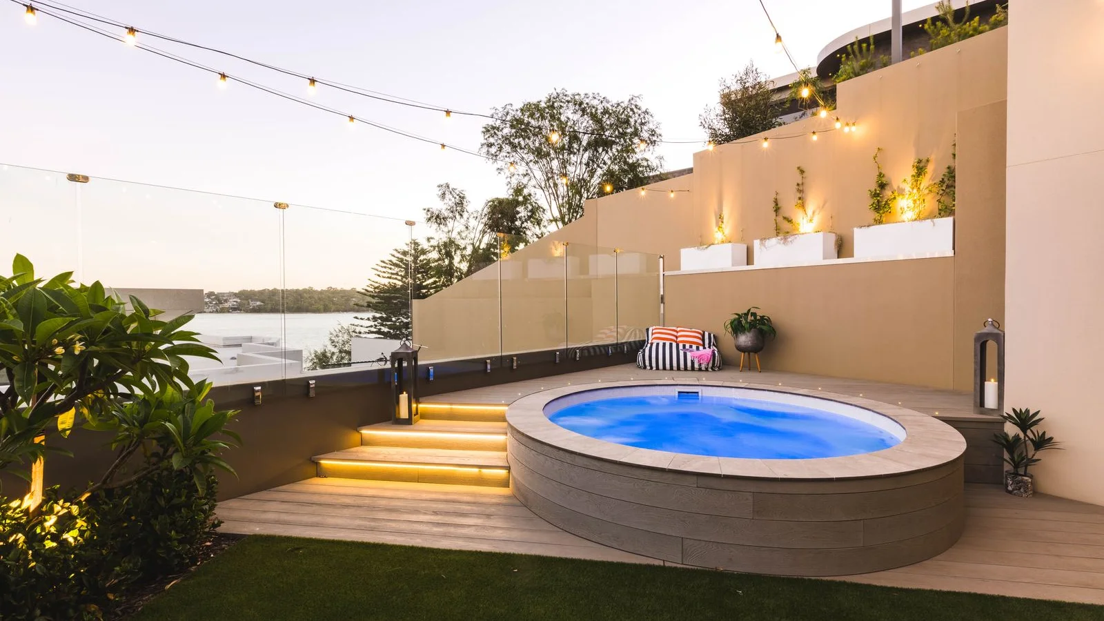 Round fibreglass plunge pool set in a timber deck with LED-lit steps and glass balustrade at dusk