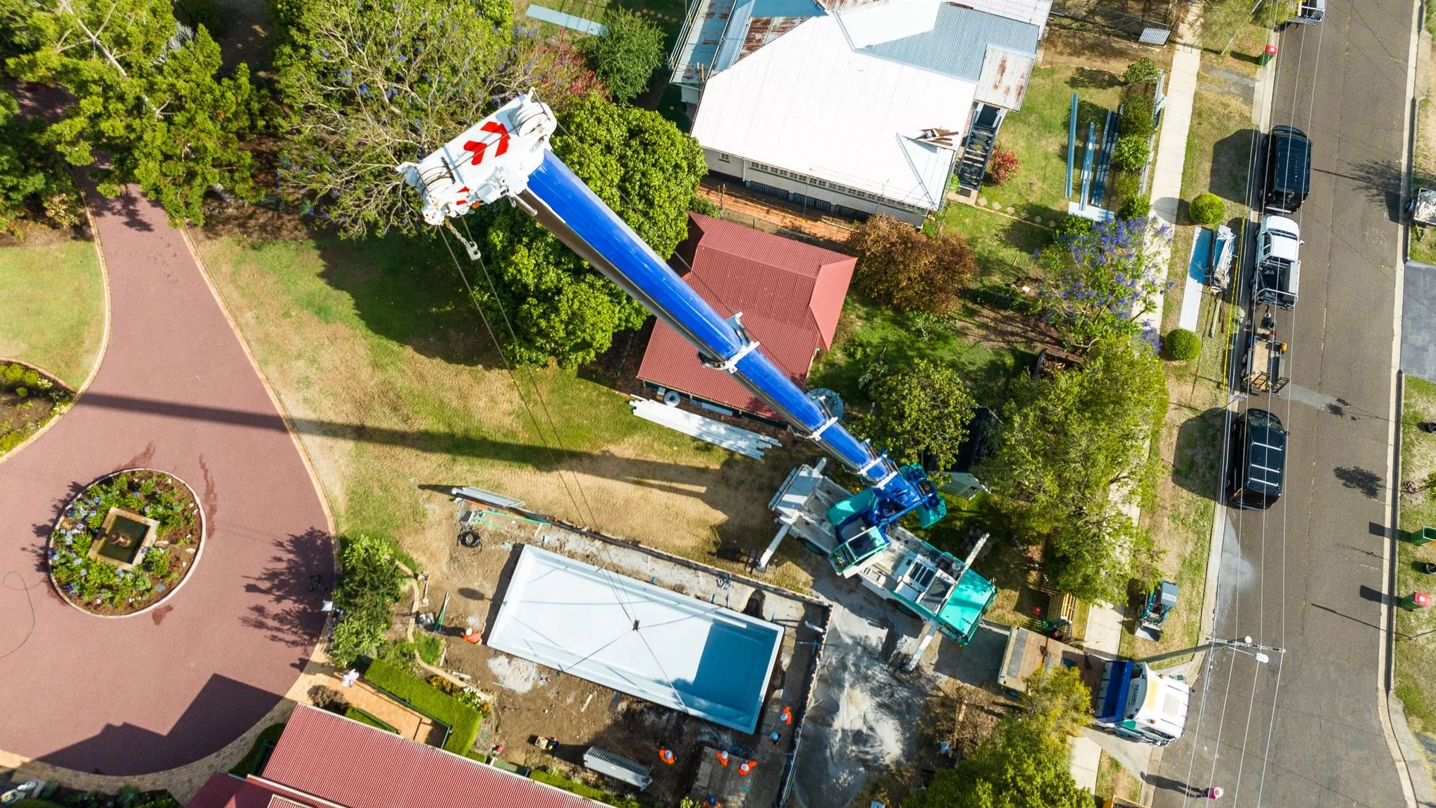 Crane lifting an Aqua Technics fibreglass pool shell over a house during an MFP Easy backyard installation