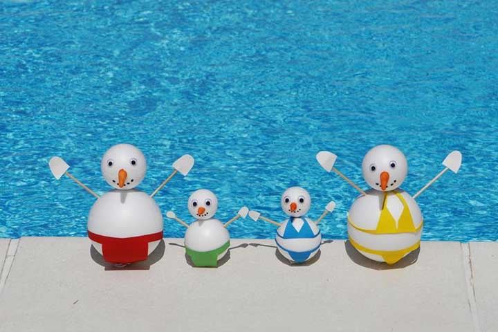 Four snowman toys with carrot noses and stick arms lined up on the edge of a bright blue pool