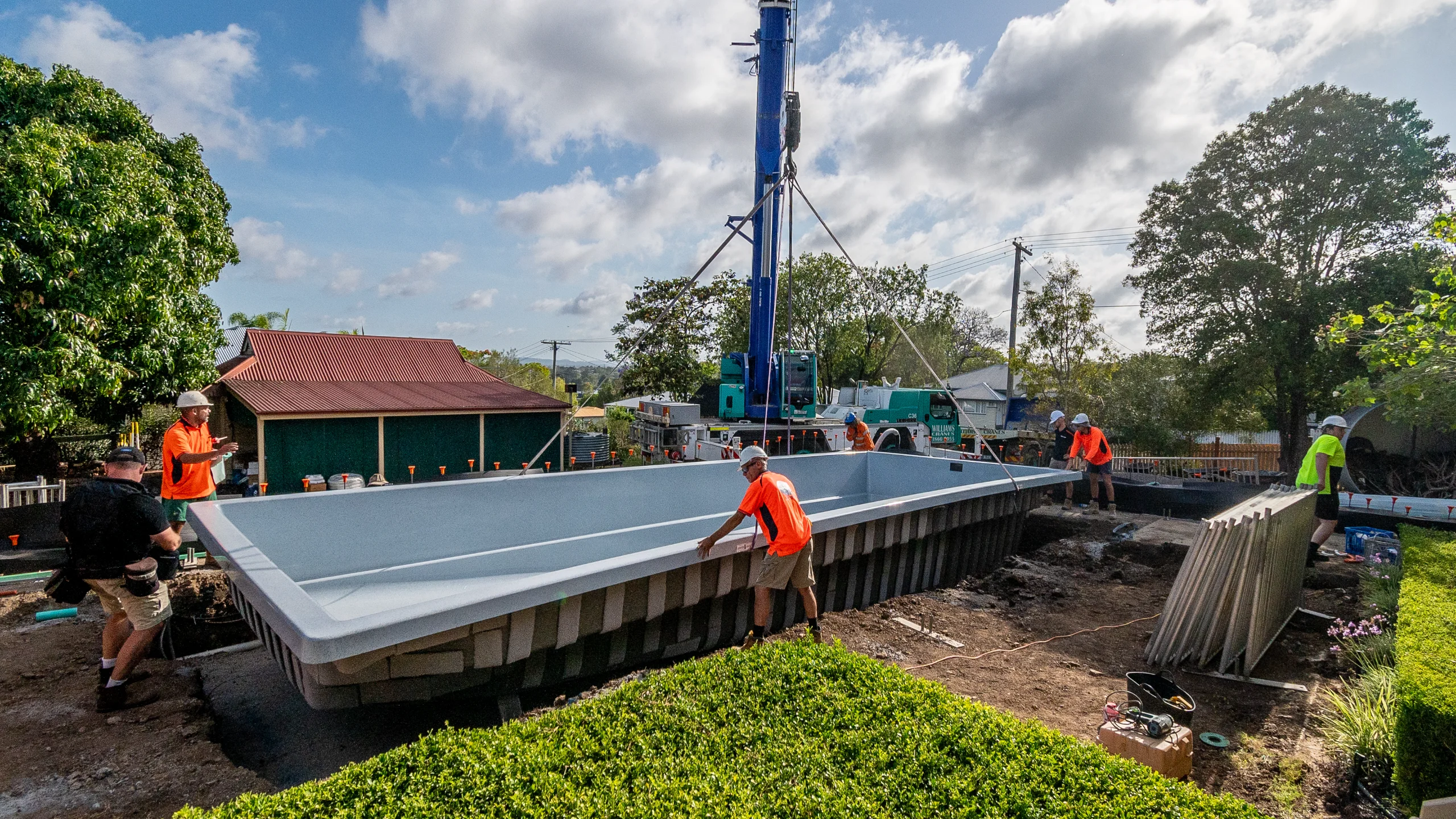 The MFP Easy team guiding a grey fibreglass pool shell into an excavated backyard with a crane