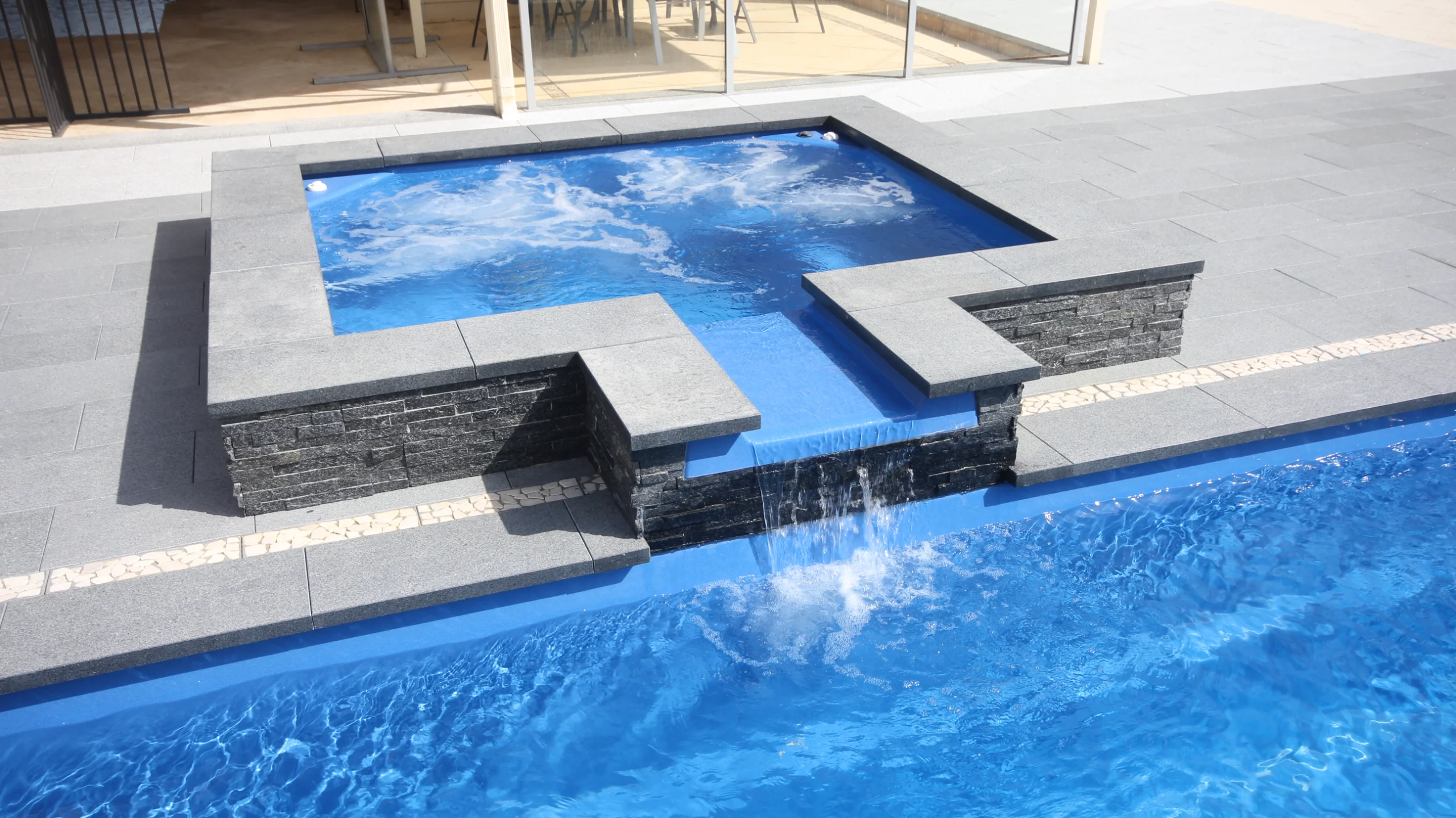 Elevated spa with raised stacked-stone waterfall feature spilling into a blue fibreglass pool below