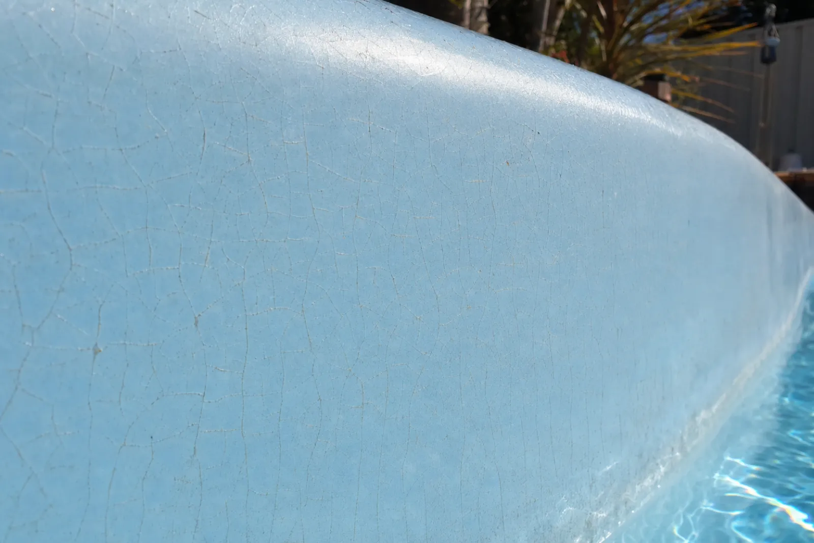 Fine hairline crazing spreading in a web across pale blue fibreglass pool gelcoat above the waterline — digital visualisation