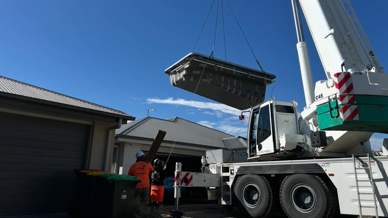 Fibreglass pool shell lifted by crane over a house as the MFP Easy team guides it into the backyard