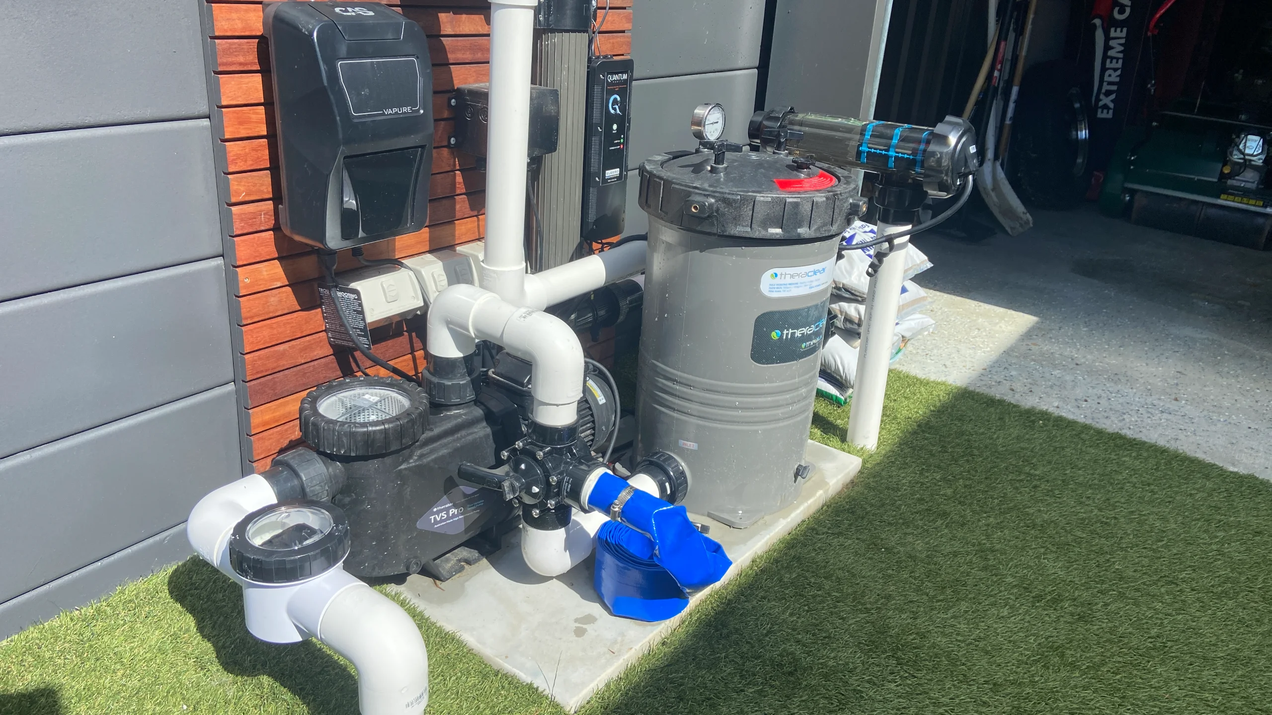 Neat pool equipment pad with pump, cartridge filter and chlorinator on a concrete slab beside a house