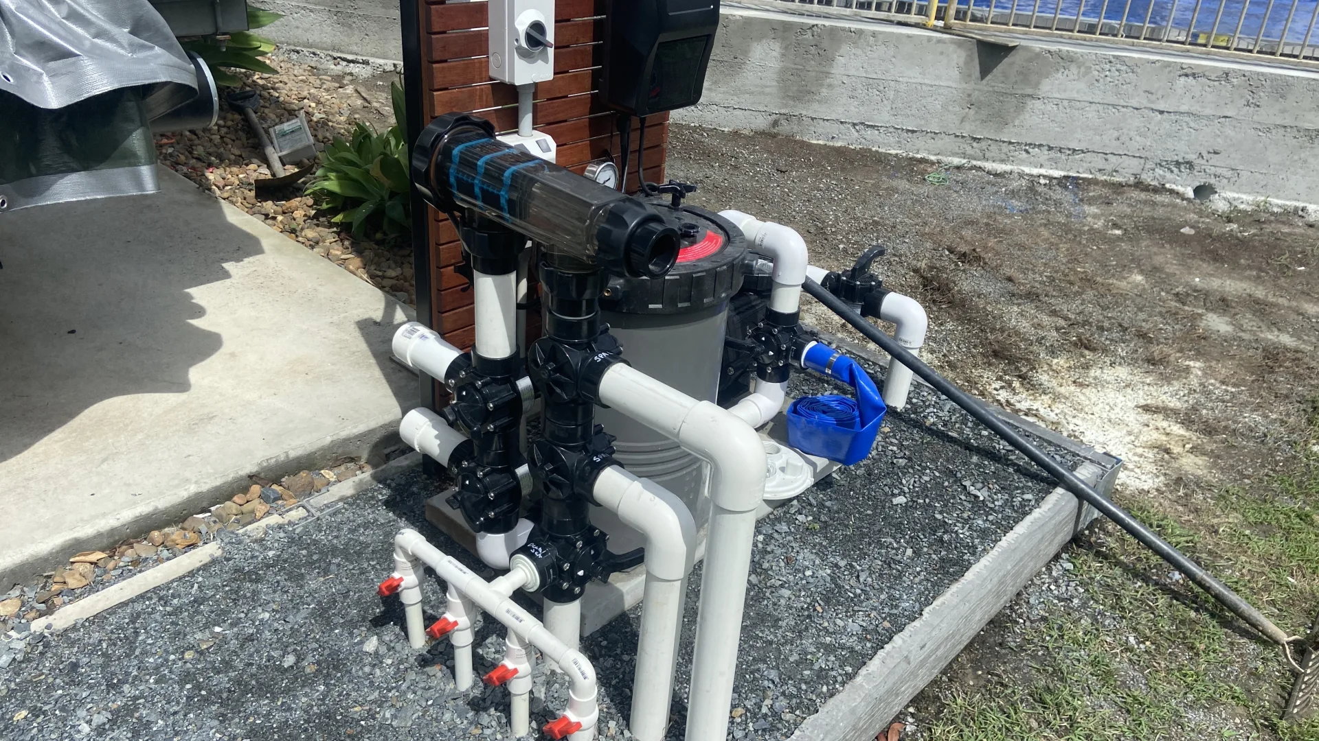Pool equipment pad with cartridge filter, chlorinator and labelled valve manifold beside a pool fence