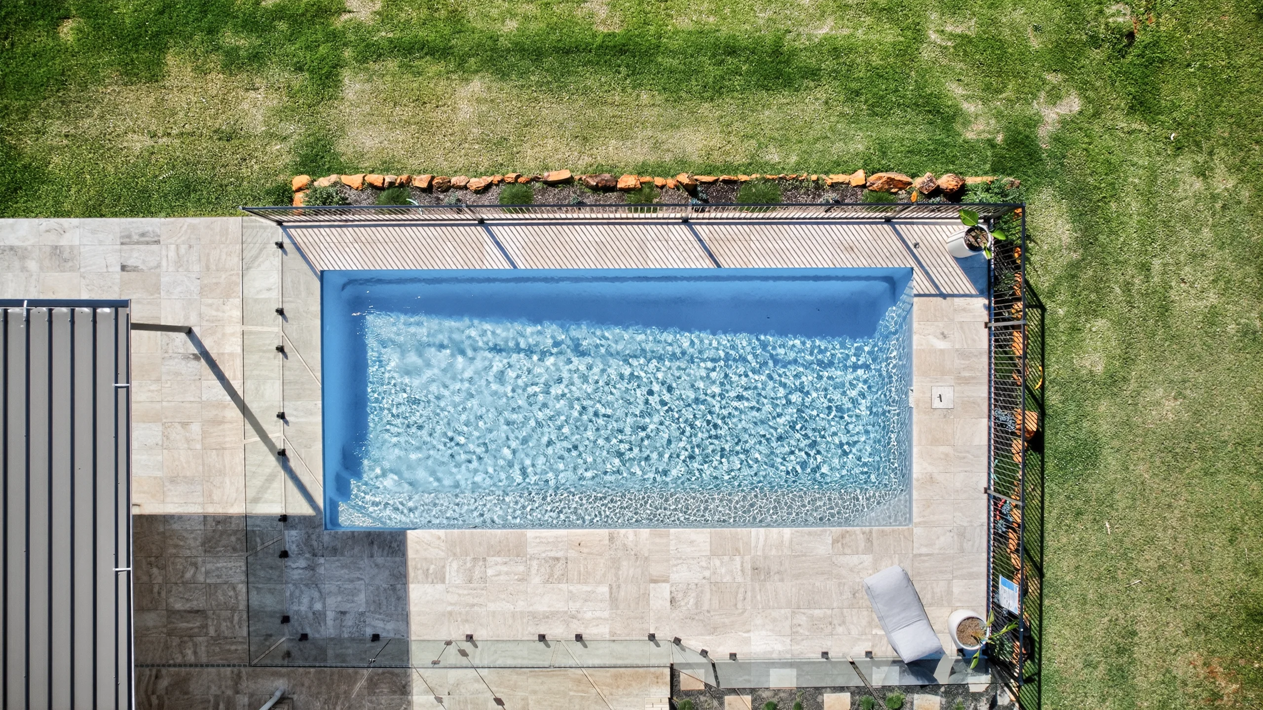 Aerial view of a completed rectangular fibreglass pool with travertine surrounds and glass fencing