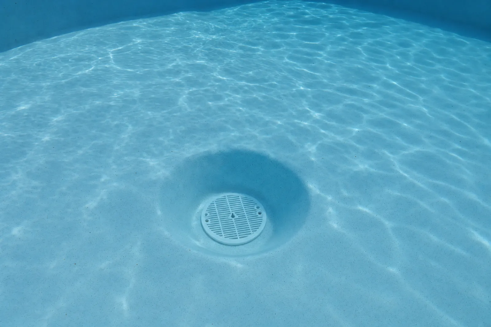 The recessed main-drain well in a fibreglass pool floor seen through clear water, where the hydrostatic valve sits — digital visualisation