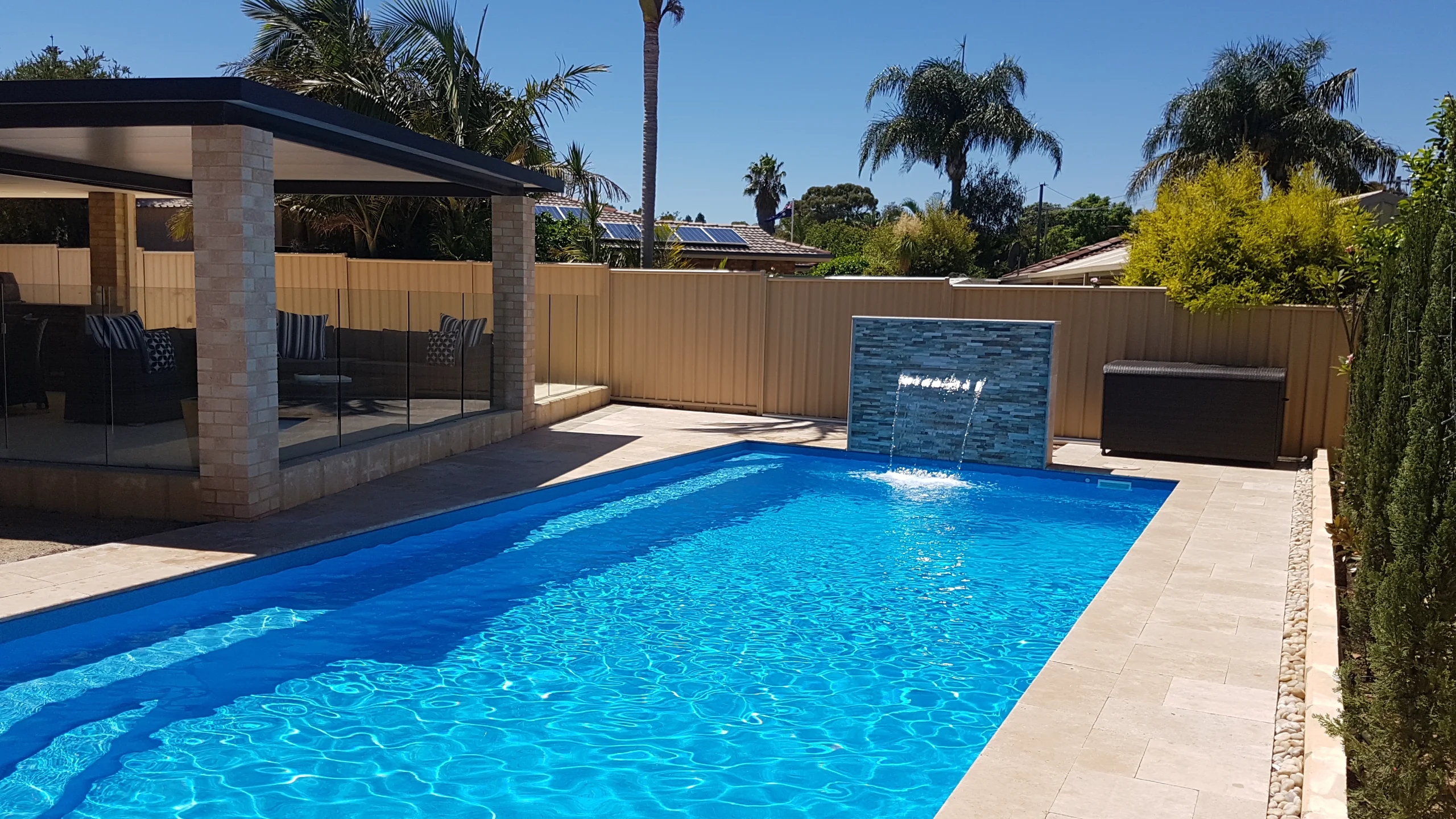 Established fibreglass pool lifespan warranty subject with grown-in surrounds, water feature and travertine paving