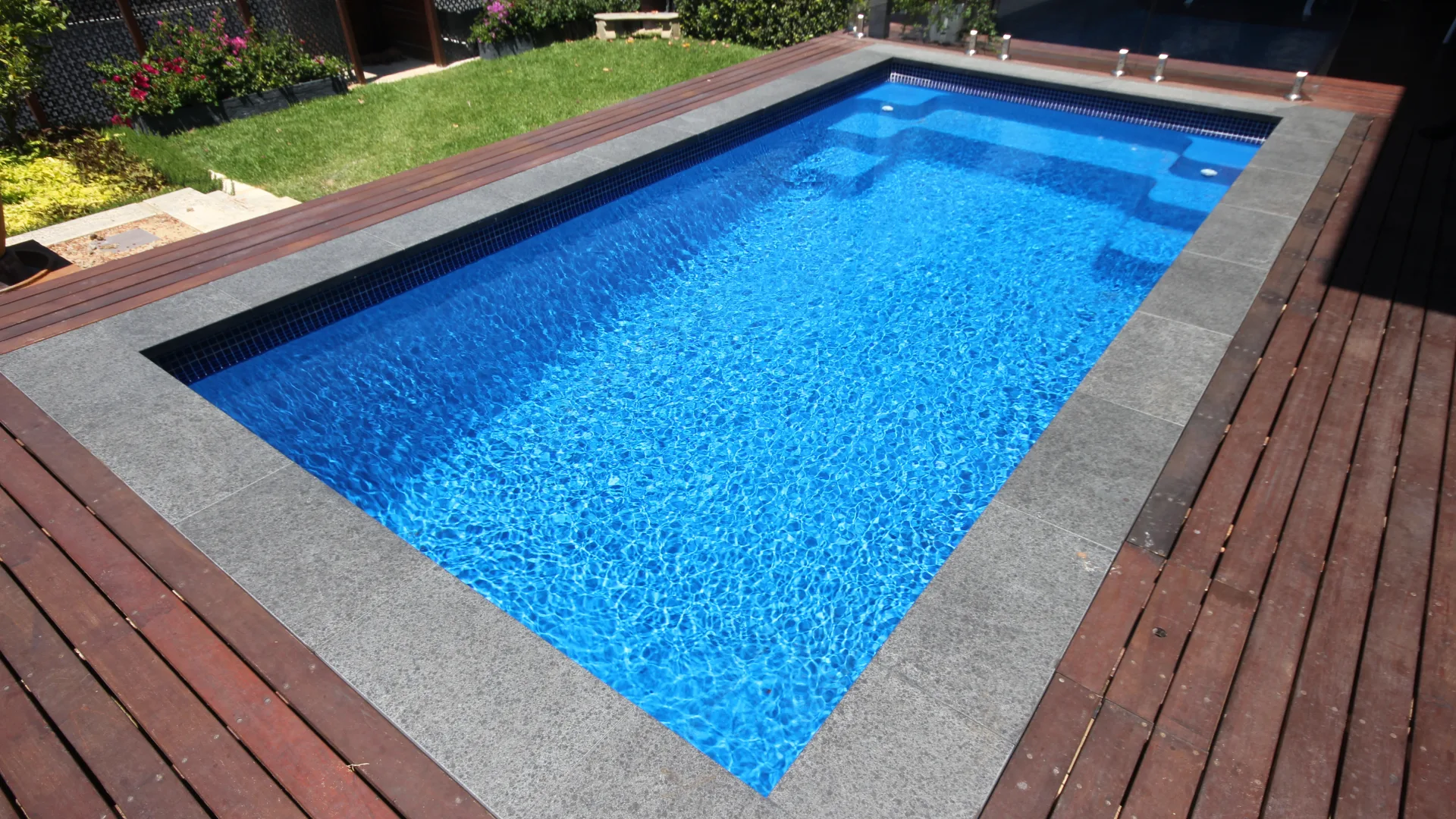 Grey stone coping around a fibreglass pool with a timber deck field beyond it