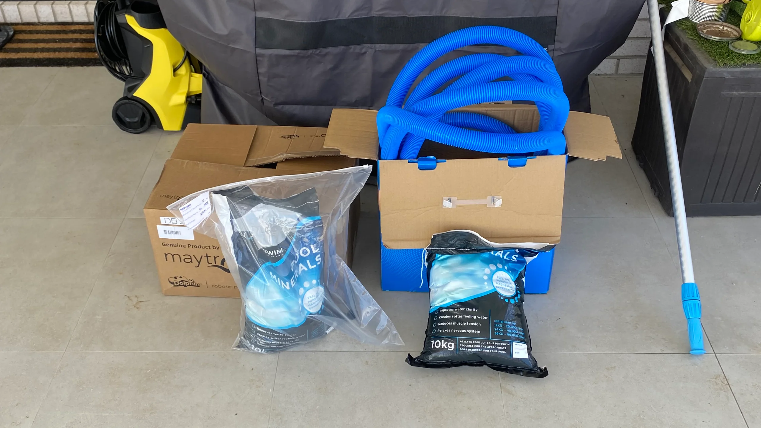 Pool chemicals like 10kg mineral bags beside vacuum hose and Dolphin box on tiled surround