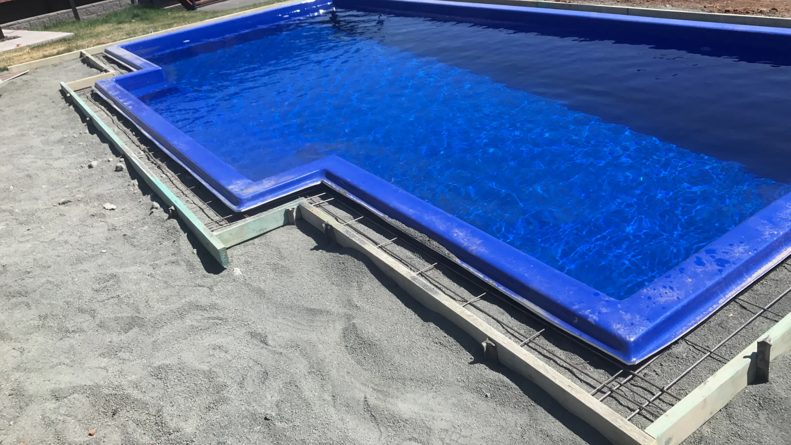 Steel reinforcement mesh and formwork set for electrician bonding beside a blue fibreglass pool