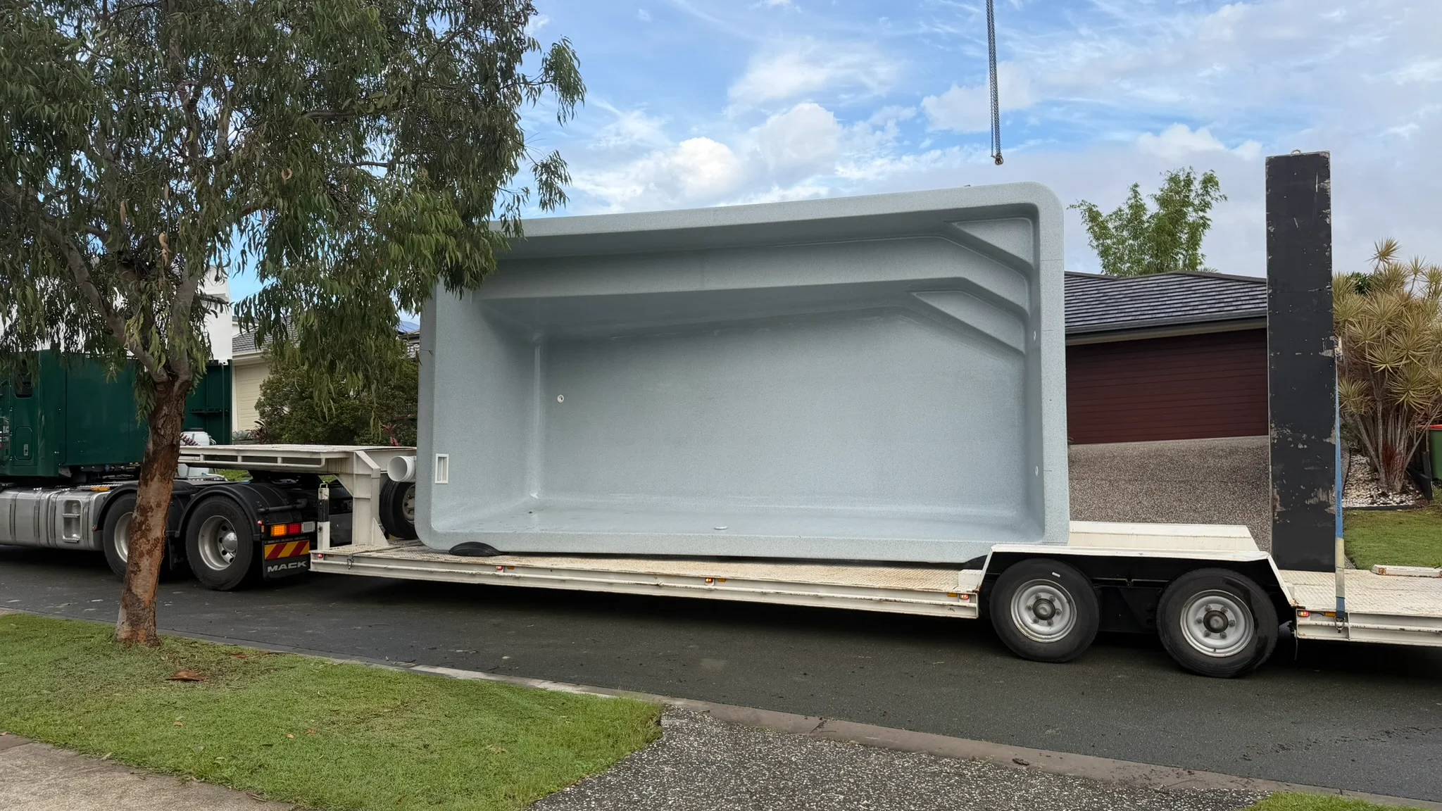 Factory-moulded Aqua Technics pool shell in pale grey on a low-loader trailer before its crane lift