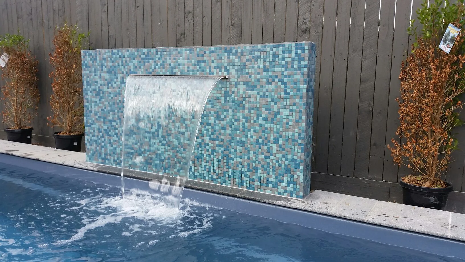 Waterline tiles in blue and grey mosaic on a fibreglass pool water feature wall with sheer cascade