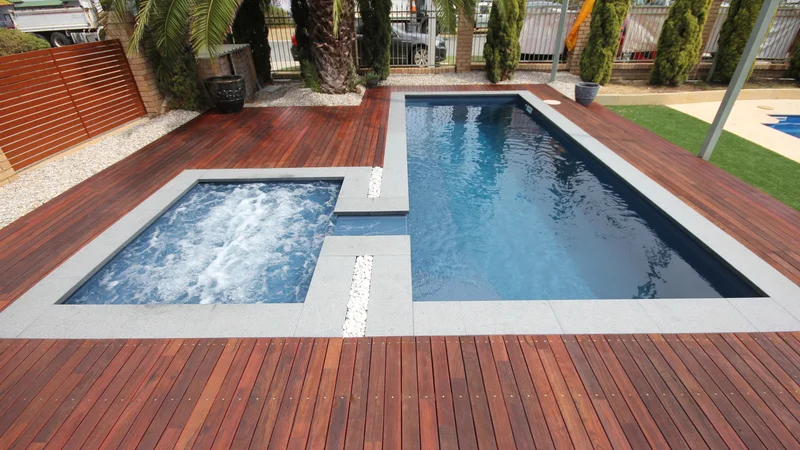 Pool resurfacing setting with two fibreglass shells framed by timber decking and pale stone coping