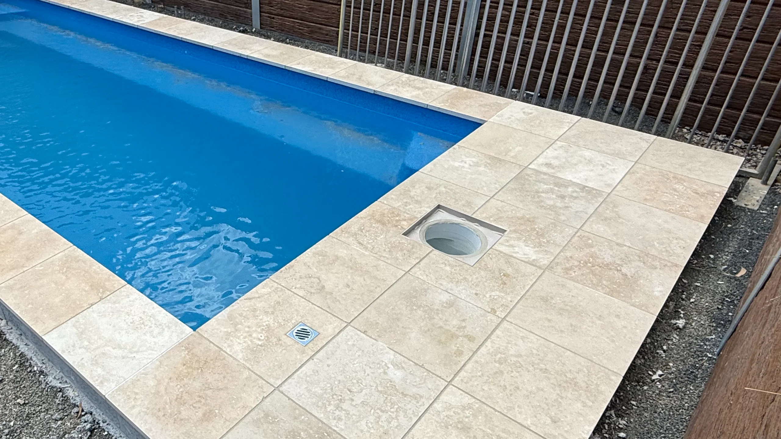 Square access lid over the white skimmer box barrel, set into paving beside a fibreglass pool