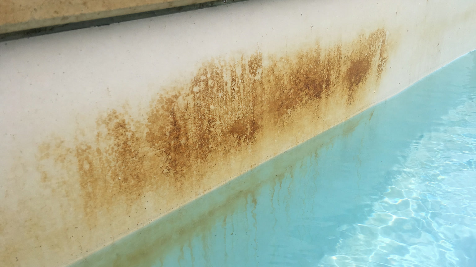 Pool stains showing rusty brown metal staining across the fibreglass gelcoat waterline above blue water