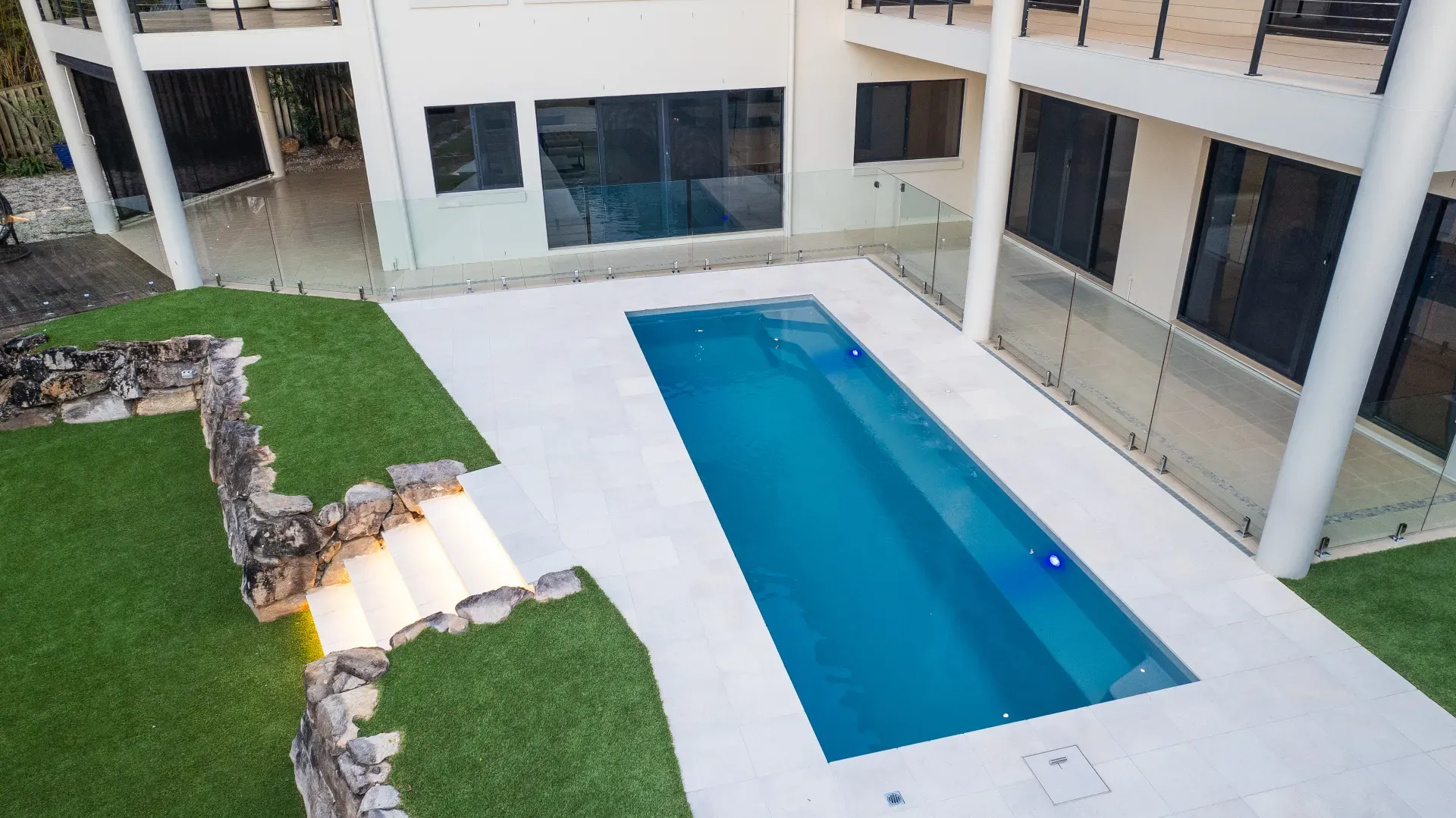 Fibreglass pool with a stone retaining wall and level paved surround on a sloping block